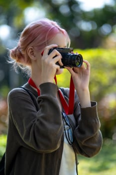 Beautiful Young artist Woman taking photo in flowers garden. Young cute girl carry the camera in the garden
