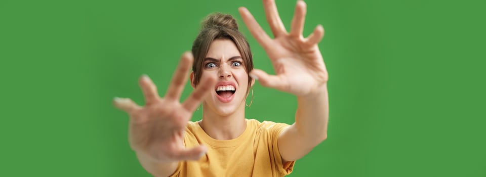 Funny emotive woman making fun face pulling hands forward to attack of grab something frowning opening mouth wanting cover face from camera, grimacing over green background photo