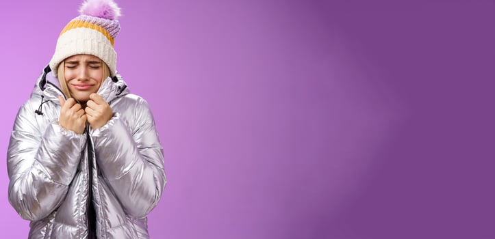 Unhappy sobbing whining cute blond girl pull jacket tight body close eyes crying freezing cold standing snowy winter resort shaking low temparature, purple background suffering discomfort photo