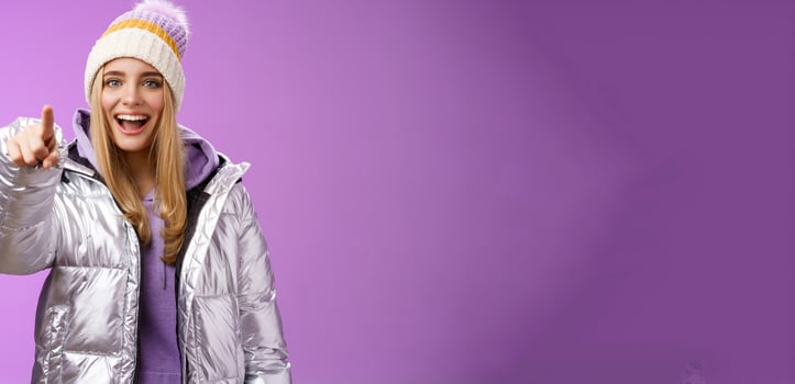 Girl make fun of clumsy friend pointing finger cruel ignorant laughing over funny amusing situation indicating camera standing happily mocking boyfriend, wearing silver winter jacket hat photo