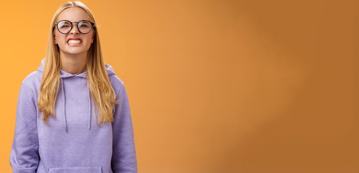 Blond girl show teeth warn can stand herself bite, fool around grimacing funny wearing purple hoodie glasses standing orange background better not mess with me, pranking friend have fun photo