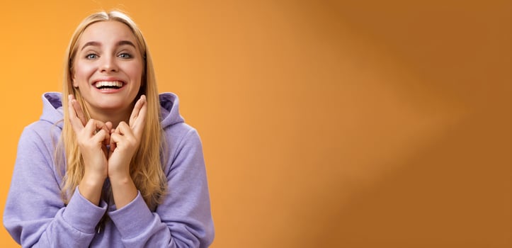 Lucky optimistic cute positive smiling blond girl grinning excited cross fingers making wish dreaming desire come true anticipating good news praying orange background waiting results photo