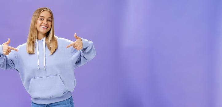 Self-assured cheerful carefree young girl with tanned skin and fair hair pointing proudly at herself bragging about own skills and achievements standing cool feeling awesome in new hoodie photo
