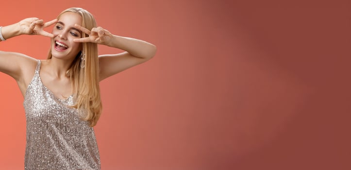 Carefree joyful beautiful fabulous blond woman having fun celebrating partying dancing happily show victory peace disco signs look aside entertained, enjoying awesome music, red background photo