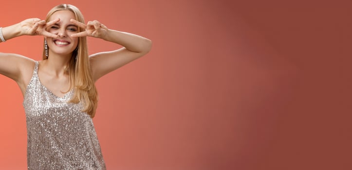 Sassy attractive stylish european girlfriend having fun celebrating birthday standing silver evening glittering dress winking cheeky make disco peace gesture near eyes enjoying party, red background photo