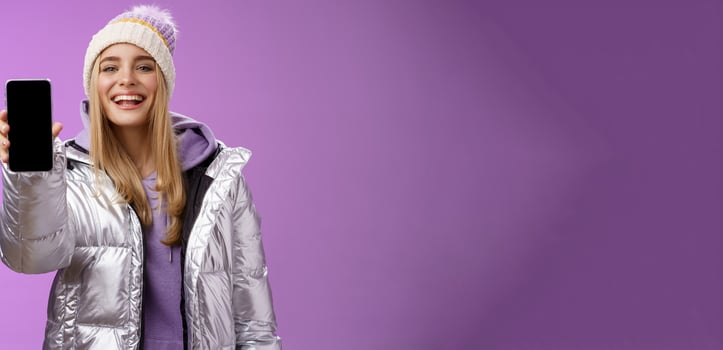 Sassy delighted cheerful blond woman recommend use app edit perfect pictures holding smartphone showing mobile phone display proudly satisfactory smile camera, standing purple background photo