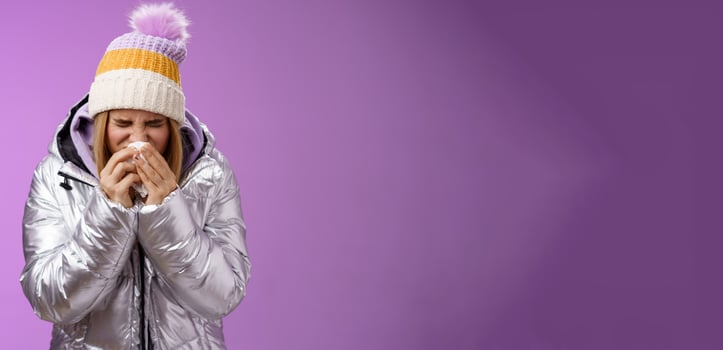 Girl runny nose sneeze tissue press napkin face got ill feeling unwell sick heading hospital standing purple background bending wearing silver stylish jacket winter hat, crying sobbing photo