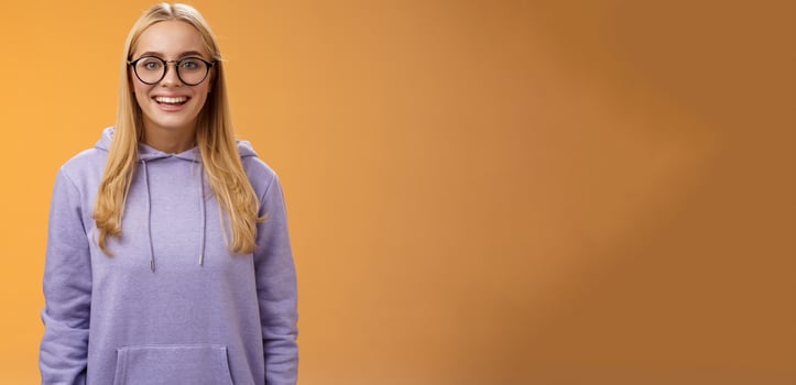 Charming female student geek smiling energized wanna participate university event grinning look excited wearing glasses purple hoodie standing amused orange background having fun photo