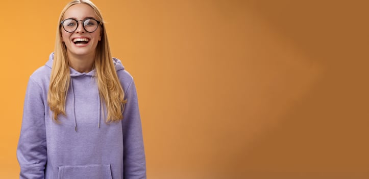 Charismatic joyful charming smiling female university straight a student in glasses purple cozy hoodie grinning laughing happily glad invited hand out classmates standing orange background photo