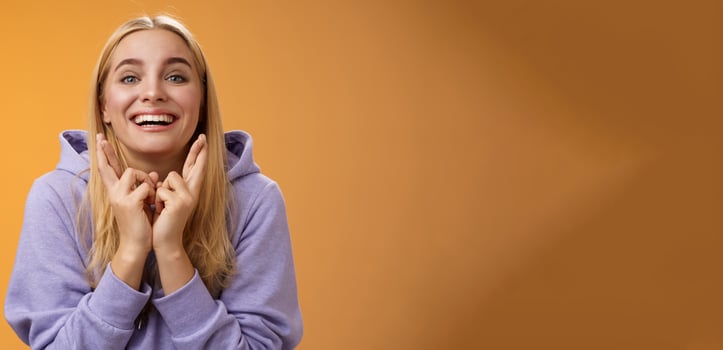 Lucky optimistic cute positive smiling blond girl grinning excited cross fingers making wish dreaming desire come true anticipating good news praying orange background waiting results photo