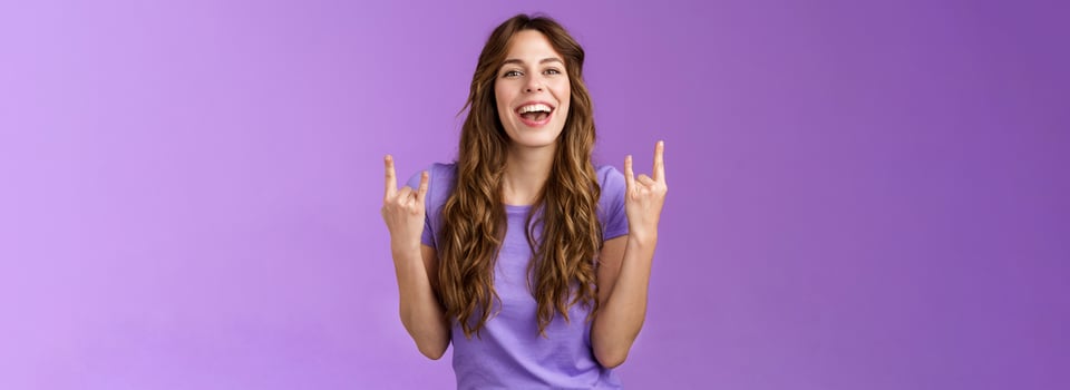 This summer holidays rock. Happy enthusiastic cheerful girl having fun enjoy awesome party weekends smiling broadly say yeah joyful make heavy-metal sign stand purple background amused photo
