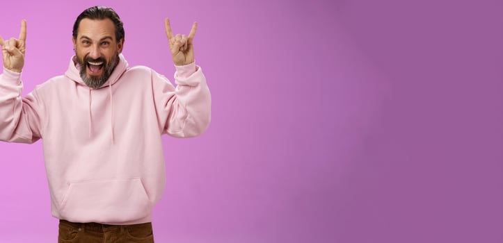 Carefree enthusiastic excited mature bearded man grey hair having fun show rock-n-roll gesture attend awesome heavy metal concert grimacing thrilled looking happy upbeat, purple background photo