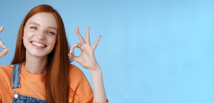 Wellbeing, happiness, perfection concept. Attractive friendly smiling joyful redhead female student show excellent okay ok gestures grinning approval agree awesome concept, satisfied blue background photo