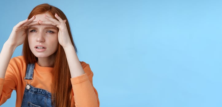 Worried clingy redhead girlfriend spying boyfriend peer from distance squinting focus sight look afar hold hands forehead cover eyes sunlight standing concentrated blue background photo