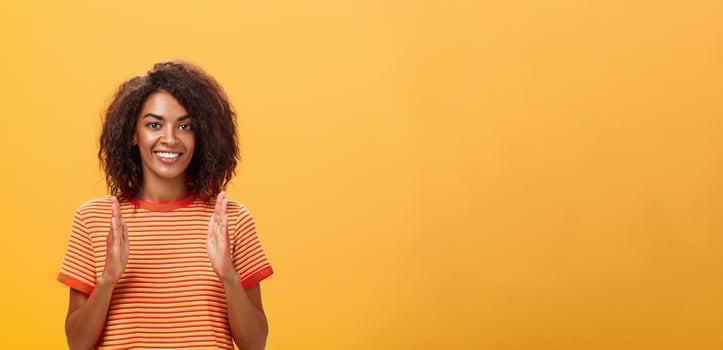 Portrait of charming friendly-looking african american woman with afro hairstyle explaining story with hands and gestures shaping object, holding palms vertical over chest and smiling at camera photo