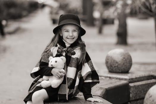 A little stylish girl in autumn clothes is sitting on a bench in the autumn city photo
