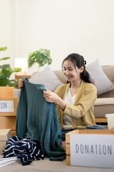 Woman asian holding donation box full with clothes and select clothes. Concept of donation and clothes recycling. Helping poor people photo