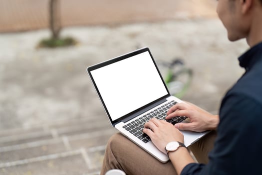 Businessman typing on mockup laptop with blank white screen at urban outside photo
