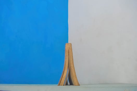 a thick book open upside down against the backdrop of a divided blue and white wall photo
