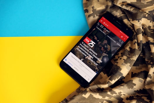 KYIV, UKRAINE - 4 MAY, 2023 TSN ukrainian news portal on smartphone screen with ukrainian flag and camouflage fabric photo
