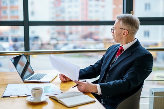 Thoughtful middle aged businessman in suit. Sitting with a laptop near the window. Man working with documents. Business concept. photo