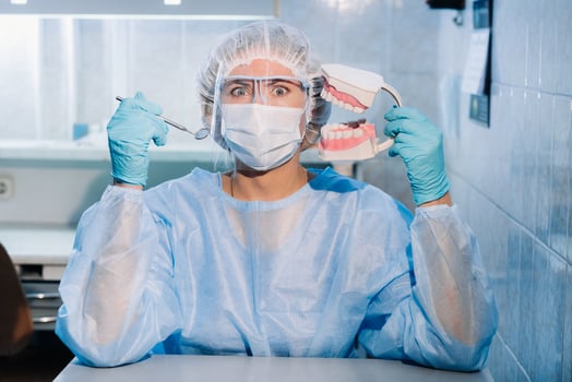 A dental doctor wearing blue gloves and a mask holds a dental model of the upper and lower jaws and a dental mirror photo