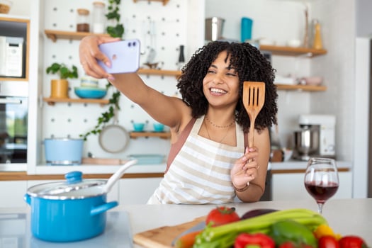 Portrait of smiling young African American woman taking selfie with smartphone while cooking in kitchen at home photo