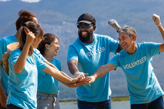 Team of young and diversity volunteer worker group enjoy charitable social work outdoor together to saving environment project wearing blue t-shirt while joining hand in power assemble unity photo