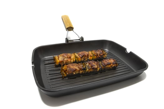 Meat and pepper skewers in a non-stick frying pan, isolated on white background. Generally a skewer is made up of pieces of meat or fish interspersed with onion, pepper, mushrooms, etc. photo