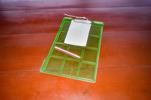 a green plastic clerk's board with a piece of paper stapled to it and a pink pen photo