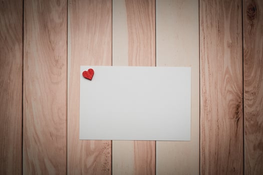 A white paper with a red heart placed on a wooden table photo