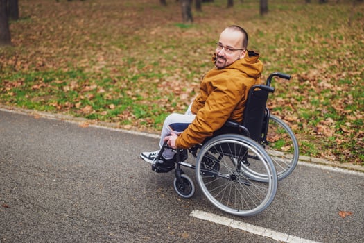 Portrait of happy paraplegic handicapped man in wheelchair in park. He is rolling on pathway. photo