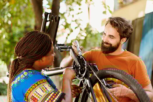 Healthy energetic caucasian man applying grease on bike chain while active young african american woman adjusts bike pedals outside. Sporty multiracial pair repairing bicycle for leisure cycling. photo