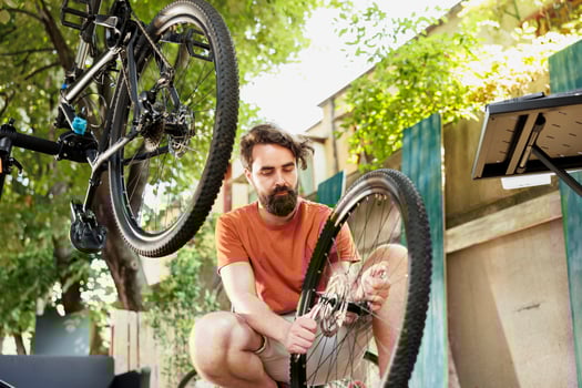 Sporty and dedicated man adjusting bicycle gears with professional equipment in home yard. Active caucasian male repairs and maintains bike components outside using specialized tools. photo