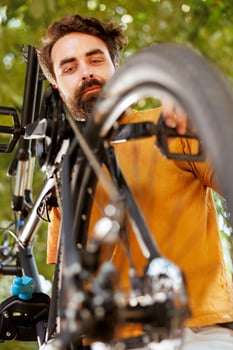 Close-up of sports-loving caucasian man working in his yard to fix bicycle parts with specialized tool. Detailed image of young male cyclist inspecting and adjusting bike wheel and pedal. photo