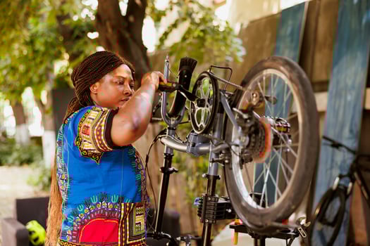 Active african american lady adjusts bike pedal and fine-tunes the gears as yearly summer maintenance. Sports-loving black woman servicing and fixing modern bicycle in home yard. photo