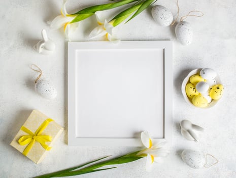 Square empty white frame, eggs, flowers, gift box, bunnies on white. Easter mockup. Top view. photo