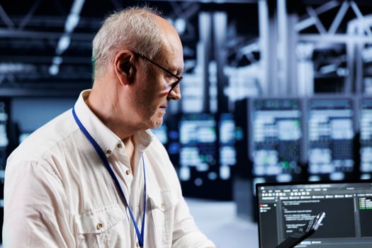 Old technician coding in technologically advanced data center using javascript language. Skilled specialist updating software on server cabinets using laptop, ensuring optimal performance and security photo
