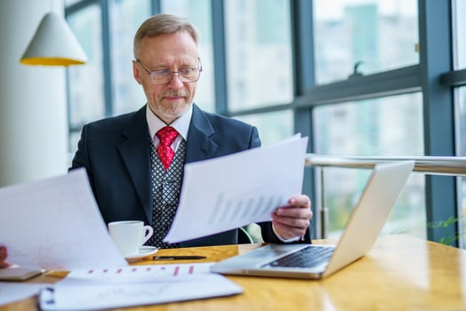 Thoughtful middle aged businessman in suit with a laptop sitting near the window working with documents, typing. photo