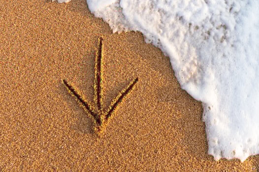 Flatlay An arrow drawn on the sand pointing to the left next to sea foam photo