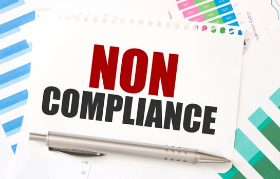 NON COMPLIANCE text on notepad with pen and graphs background. Regulatory and legal concept photo