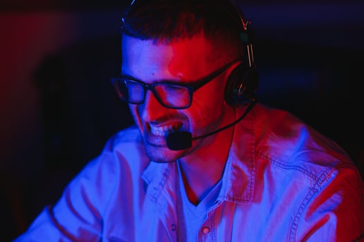 Professional Gamer Plays Video Game on His Computer. He's Participating in Online Cyber Games Tournament or in Internet Cafe. He Wears Glasses and Talks into Microphone. photo