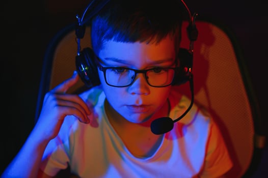 Child online broadcasts computer game, boy streams in headphones on rgb lighting background photo