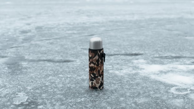 Thermos in a khaki case standing on a frozen lake. Concept hot drink in cold weather, winter fishing, hiking photo