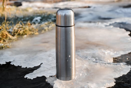 Thermos standing on ice, close-up. Vacuum steel flask for hiking. Travel concept, warming drink in winter. photo