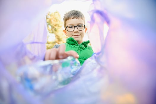 Environmental conservation concept.Little boy collects garbage and plastic bottles in the street to throw them in the trash bin photo