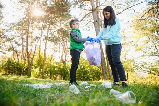 Woman volunteer and little boy picking up the plastic garbage and putting it in biodegradable trash-bag outdoors. Ecology, recycling and protection of nature concept. Environmental protection. photo
