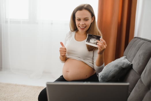 selective focus of cheerful pregnant woman showing ultrasound photos while having video call