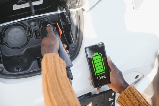 Close up of male hand holding electric charging plug for luxury red car. African businessman charging his auto on station. Eco friendly transport. photo