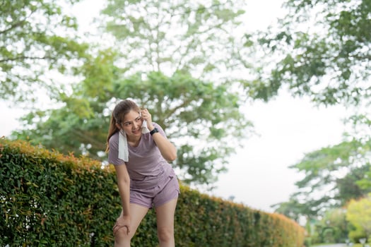 Asian woman taking a moment to catch her breath after tired workout in park photo
